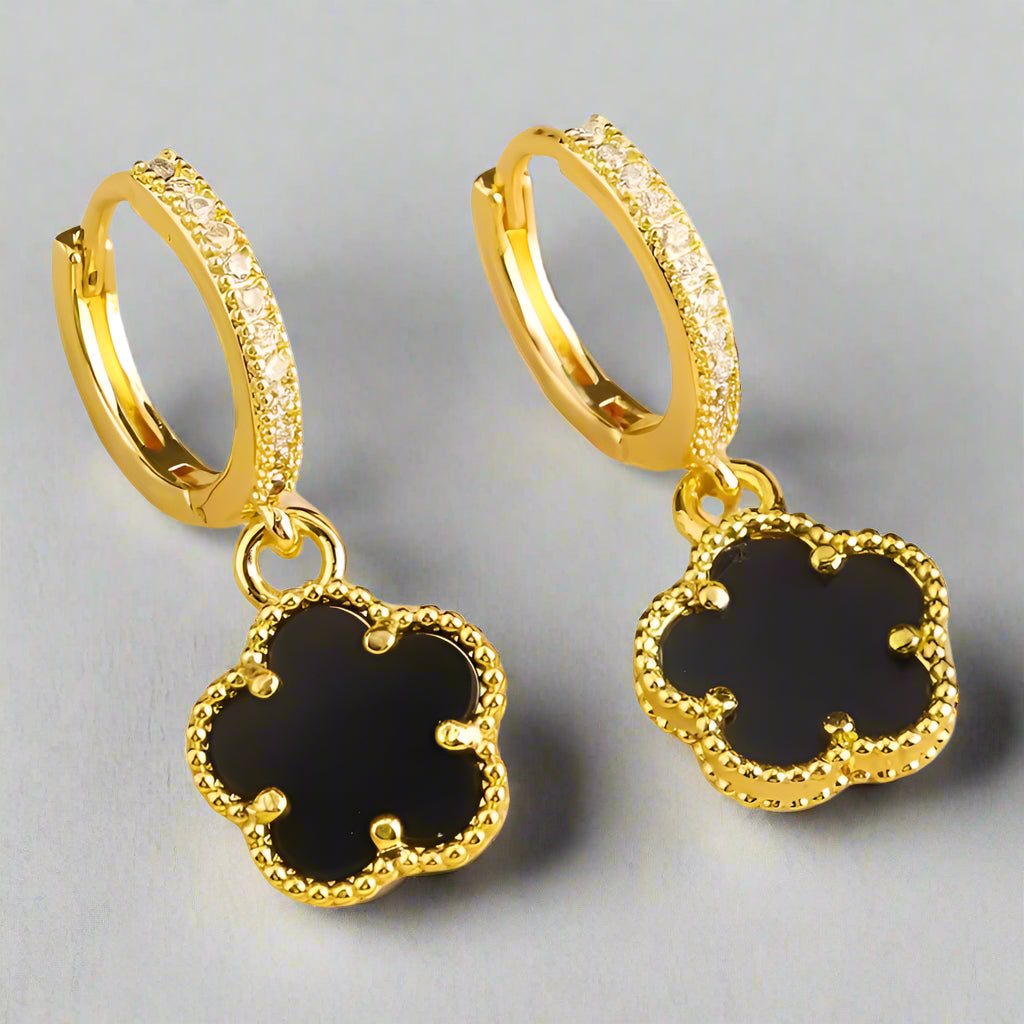Gold hoop earrings with black clover-shaped charms on a white background