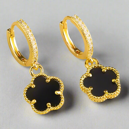 Gold hoop earrings with black clover-shaped charms on a white background