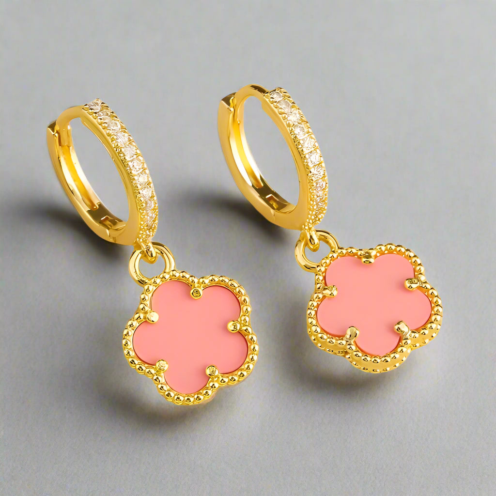 Gold hoop earrings with pink clover-shaped charms on a white background