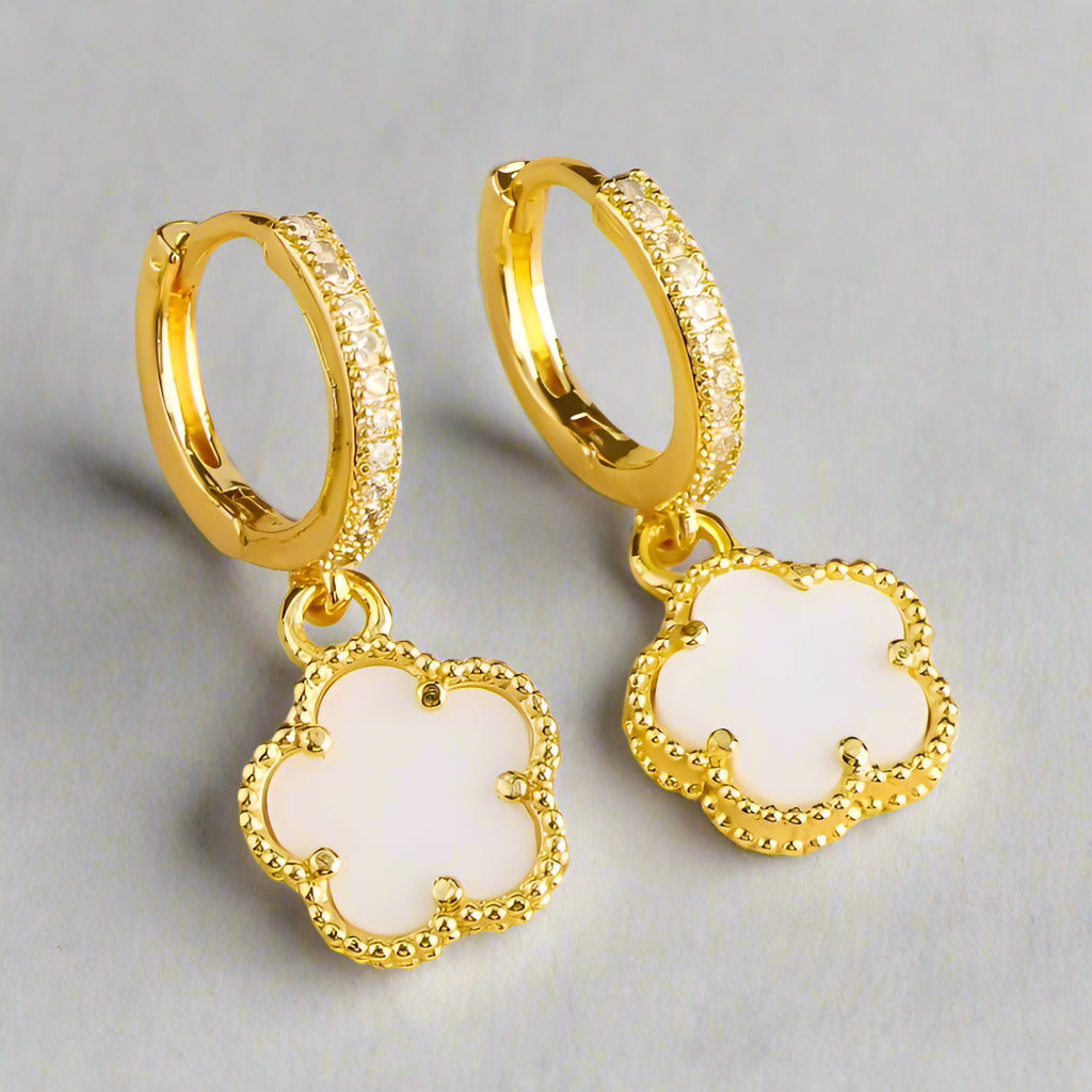 Gold hoop earrings with white clover-shaped charms on a white background