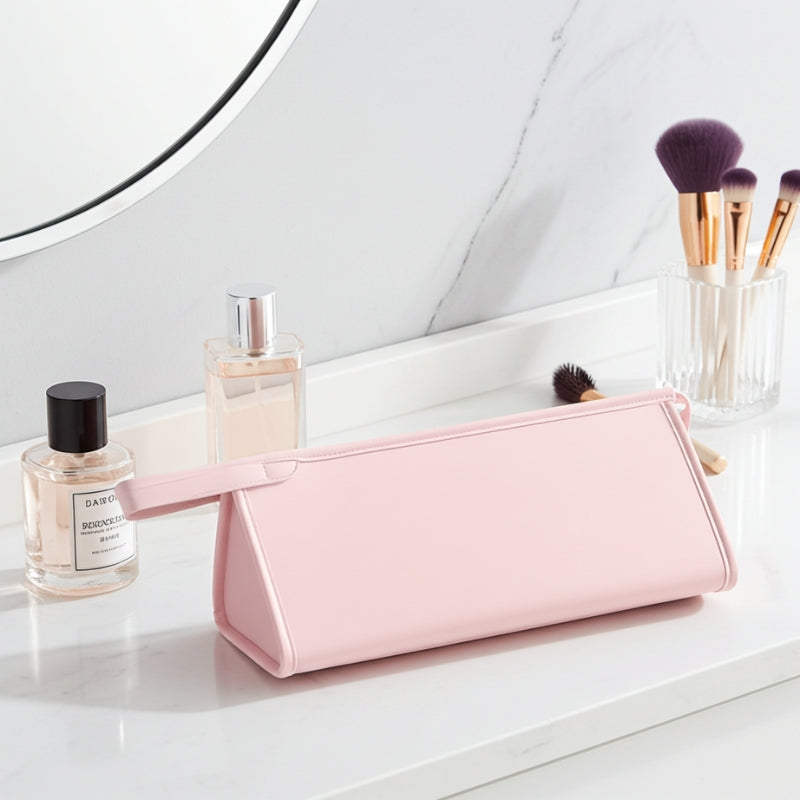 Pink toiletry bag on a bathroom counter with perfume bottles and brushes.