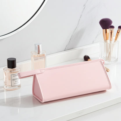 Pink toiletry bag on a bathroom counter with perfume bottles and brushes.