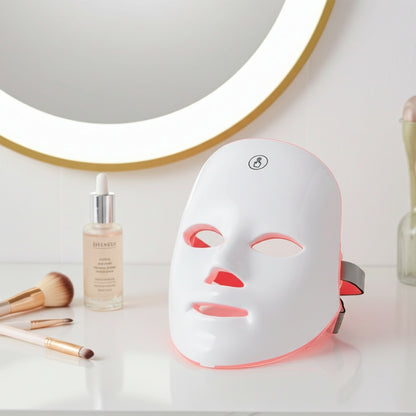 LED face mask on a white surface with cosmetic items and a mirror in the background